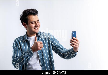 Gros plan d'un modèle de jeune adulte à la peau marron, effectuant un appel vidéo avec un smartphone sur un arrière-plan blanc isolé. Banque D'Images