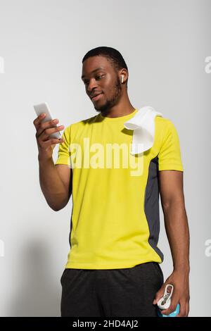 sportif afro-américain avec écouteur dans l'oreille et smartphone sur fond gris Banque D'Images