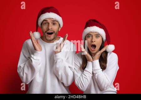 Ventes de Noël.Homme et femme surpris à Santa Hats s'exclamant avec enthousiasme Banque D'Images