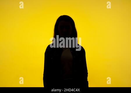 Pas de nom, personne anonyme cachant le visage dans l'ombre, identité humaine.Portrait de la silhouette d'une femme inconnue debout seule, prise en studio en intérieur, isolée sur fond jaune Banque D'Images