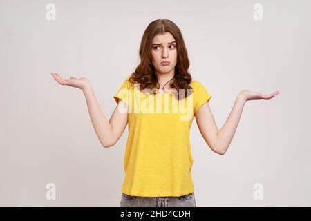 Je ne sais pas, qui s'en soucie.Portrait d'une adolescente sans indice confus attrayante en t-shirt jaune haussant les épaules, ne faisant aucun geste d'idée, quoi que ce soit.Prise de vue en studio isolée sur fond gris. Banque D'Images