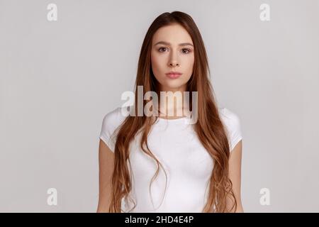 Portrait d'une femme très attirante, debout, regardant l'appareil photo, se sent confiante et sûre d'elle-même, exprimant son sérieux, en portant un T-shirt blanc.Prise de vue en studio isolée sur fond gris. Banque D'Images