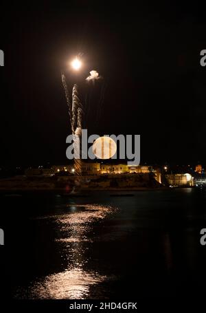 Pleine lune sur la ville de Kalkara à Malte avec de beaux feux d'artifice et son reflet dans la mer pendant la nuit.Photographie de nuit.Feux d'artifice à Malte.Feux d'artifice Banque D'Images