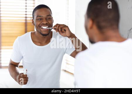 Happy Young African American Man se brossant les dents avec une brosse à dents dans la salle de bains Banque D'Images