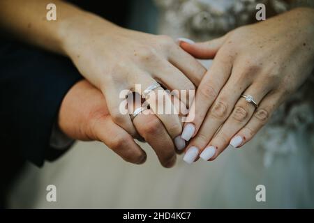 Gros plan sur une mariée et un marié tenant les mains et montrant leurs anneaux Banque D'Images