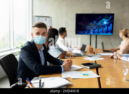 Santé en milieu de travail.Équipe d'affaires multiethnique portant des masques médicaux ayant une réunion au bureau Banque D'Images