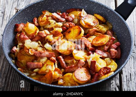 Gros plan de Bratkartoffeln, pommes de terre frites allemandes au bacon et à l'oignon dans une poêle sur une table rustique en bois Banque D'Images