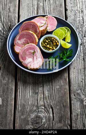 Filet de porc farci à l'ail italien et à l'herbe sur une assiette de sauce pesto et citron vert, vue verticale depuis le dessus Banque D'Images