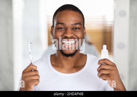 Concept de soins buccaux.Homme noir souriant avec brosse à dents et dentifrice dans les mains Banque D'Images