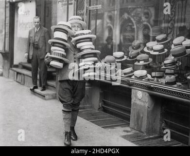 Vintage début 20th siècle photo de presse: Jeune homme à l'extérieur de la boutique de chapeau avec des plaisanciers Banque D'Images