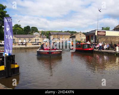 Les touristes regardant une barge de cargaison qui passe avec un bateau à narrowboat amarré à côté, et appréciant le soleil au bassin du canal de Skipton dans le Yorkshire, en Angleterre. Banque D'Images