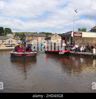 Les touristes regardent une barge de cargaison qui passe et profitent du soleil au bassin du canal de Skipton dans le Yorkshire, en Angleterre. Banque D'Images