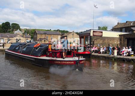 Les touristes regardent une barge de cargaison qui passe et profitent du soleil au bassin du canal de Skipton dans le Yorkshire, en Angleterre. Banque D'Images