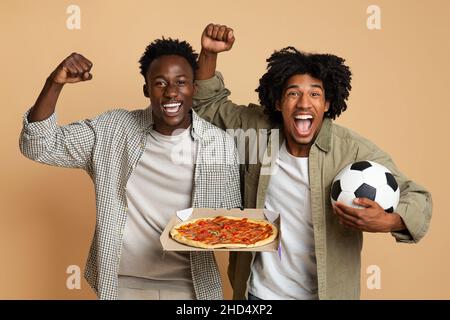 Deux fans de Black football enthousiastes tenant le ballon de football et la pizza Banque D'Images