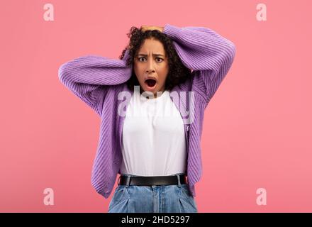 Des nouvelles choquantes.Femme afro-américaine émotive tenant la tête dans la panique sur fond rose studio Banque D'Images