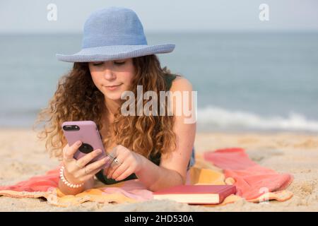 jeune femme à la plage sur une serviette regardant le téléphone portable. Banque D'Images