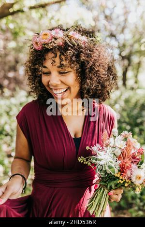 Gros plan d'une femme noire souriant dans une zone boisée tout en tenant des fleurs Banque D'Images