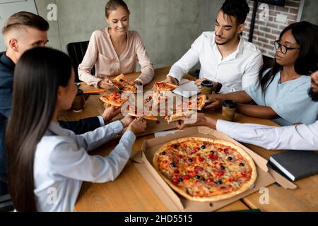 Groupe de collègues multiethniques appréciant une pause déjeuner au bureau, manger pizza ensemble Banque D'Images