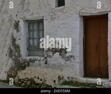 Ancienne façade de maison rurale traditionnelle avec une porte en bois et une fenêtre en bois gris sur un mur blanchi à la chaux à Leonidio, Arcadia Grèce. Banque D'Images