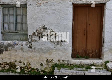 Ancienne façade de maison rurale traditionnelle avec une porte en bois et une fenêtre en bois gris sur un mur blanchi à la chaux à Leonidio, Arcadia Grèce. Banque D'Images