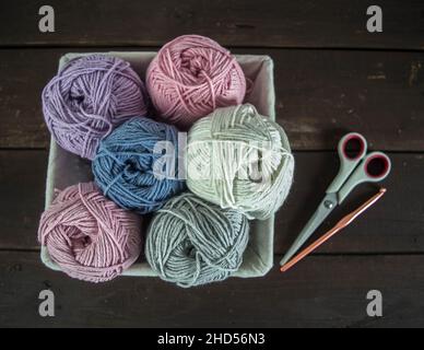 boules de laine de couleur pastel dans un panier avec ciseaux et crochet sur bois brun foncé moulus à la main Banque D'Images