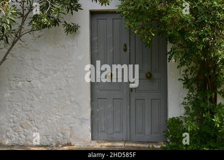 Ancienne maison rurale traditionnelle porte en bois grise antique sur un mur blanchi à la chaux avec une usine de jasmin grimpant à Leonidio, Arcadia Péloponnese, Grèce. Banque D'Images