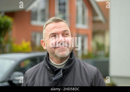 Homme d'âge moyen regardant avec un sourire amusé alors qu'il se tient en ville dans une veste chaude dans un portrait de gros plan Banque D'Images