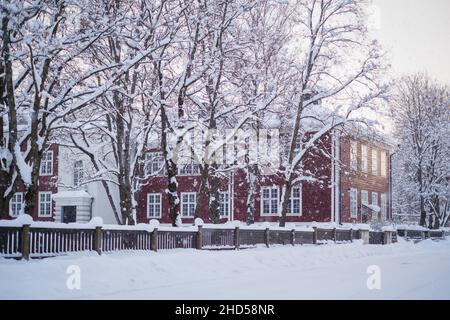 Neige abondante dans une rue enneigée de la ville avec un beau vieux bâtiment en bois en arrière-plan.Beau temps d'hiver froid. Banque D'Images