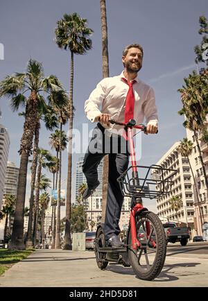 Un homme heureux en tenue de formalwear, e-scooter sur le trottoir, e-scoting Banque D'Images