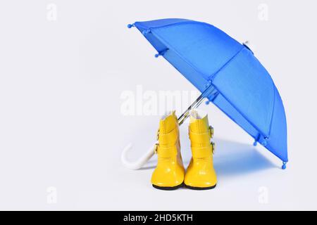 Concept de pluie avec parapluie bleu et bottes en caoutchouc jaune Banque D'Images