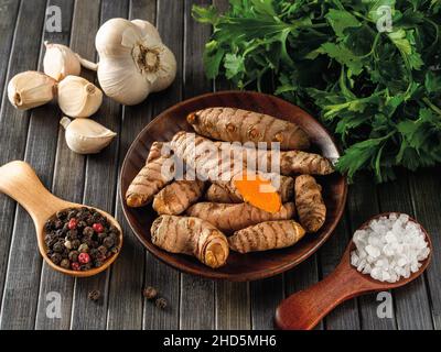 Racines de curcuma turmérique biologique crues, gousses d'ail, grains de poivre, sel de mer et persil frais sur une table en bois noir.Épices indiennes, assaisonnements, curry Banque D'Images