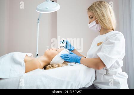 Médecin cosmetologiste fait l'échographie professionnelle de nettoyage de la peau du visage d'une belle femme dans un salon de beauté.Procédure de décollement de la face Banque D'Images