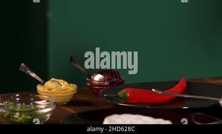 Gros plan de différents ingrédients pour cuisiner sur une table en bois sur fond de mur vert.Piment, canneberge, mayonnaise et moutarde sa Banque D'Images