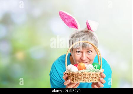 Femme âgée qui se trouve derrière le panier avec des œufs de Pâques sur fond naturel Banque D'Images