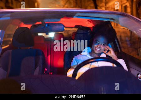 Une femme afro-américaine heureuse est assise en voiture derrière le volant, souriante femme noire au siège du conducteur Banque D'Images