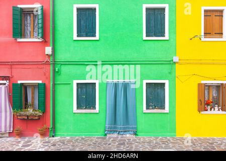 Gros plan d'une façade en plâtre de deux étages aux couleurs vives avec fenêtres avec pots de fleurs et une porte, la plus à gauche rouge, le centre vert, la plus à droite jaune Banque D'Images