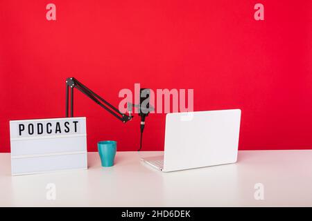 Studio d'enregistrement de radio de podcast, avec ordinateur, microphone et boîte lumineuse avec le mot podcast, sur fond rouge.Podcasting, concept de diffusion Banque D'Images