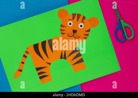 Vue de dessus de l'applique de tigre orange faite à la main sur papier vert et des ciseaux sur fond bleu et rose Banque D'Images