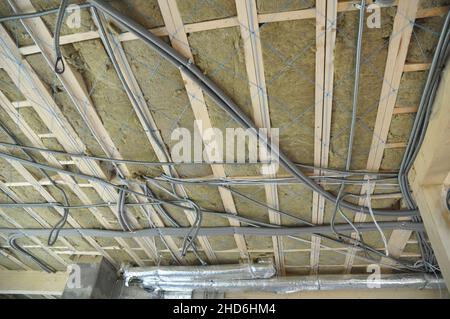 Isolation en laine minérale de plafond avec tuyaux de ventilation et câblage électrique, câbles d'alimentation en conduit pvc installés sur le plafond pendant la maison de récemm Banque D'Images