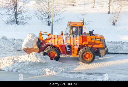 23 décembre 2021.Région de Kemerovo, Russie.Un gros tracteur orange nettoie la neige de la route et la charge dans le camion.Nettoyage et nettoyage de la route Banque D'Images