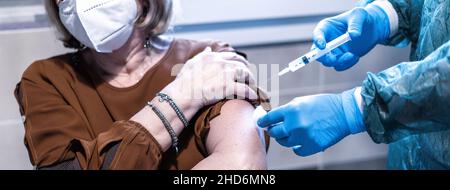 Bannière horizontale avec le médecin en costume de noisette donnant au patient un vaccin pour la maladie de coronavirus - femme sénior portant un masque facial de protection faisant vaccin Banque D'Images