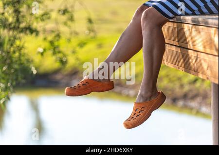 une femme est assise sur le bord d'une passerelle et balance ses jambes sur l'eau du lac Banque D'Images
