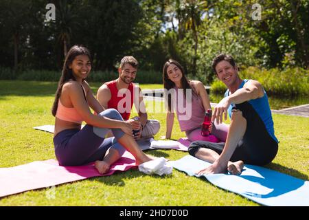 Portrait d'hommes et de femmes souriants assis sur des tapis d'exercice après l'entraînement dans le parc Banque D'Images