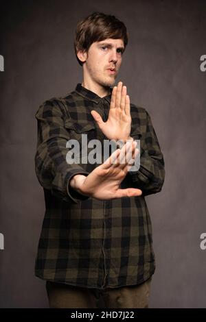Jeune beau grand homme blanc mince avec les cheveux bruns gardant la distance avec chemise en flanelle sur fond gris Banque D'Images