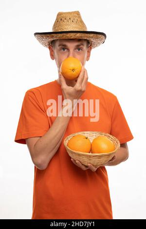 Jeune beau grand homme blanc mince avec cheveux bruns couvrant la bouche avec orange dans chemise orange avec chapeau de paille isolé sur fond blanc Banque D'Images