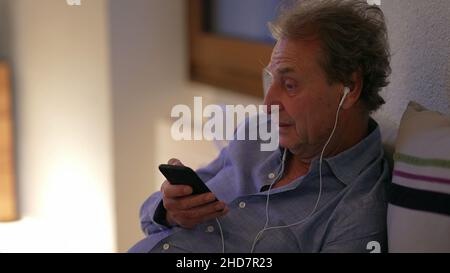 Homme senior parlant au téléphone avec des écouteurs à la maison.Personne âgée parle sur téléphone portable Banque D'Images