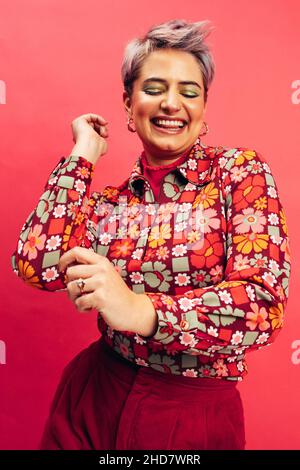 Descendre en studio.Bonne jeune femme dansant et souriant avec joie tout en se tenant sur un fond rouge.Jeune femme aux cheveux teints havin Banque D'Images