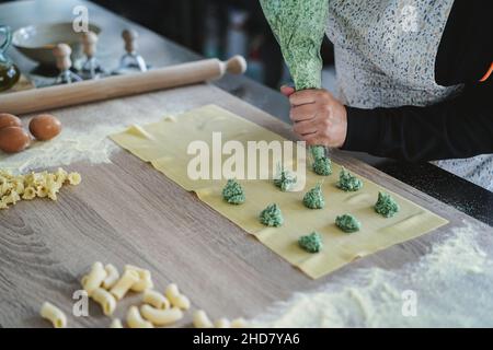 Femme prépare des raviolis frais à l'intérieur de l'usine de pâtes - Focus sur la main tenant le sac de pâtisserie Banque D'Images