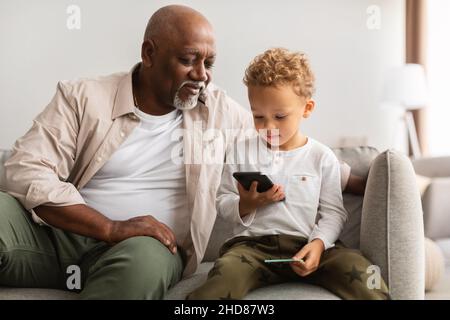 Grand-père et petit-fils noirs utilisant un téléphone portable assis sur la table intérieure Banque D'Images