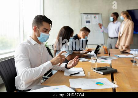Nouvelle normale.Employé arabe masculin portant un masque médical utilisant un désinfectant sur le lieu de travail Banque D'Images